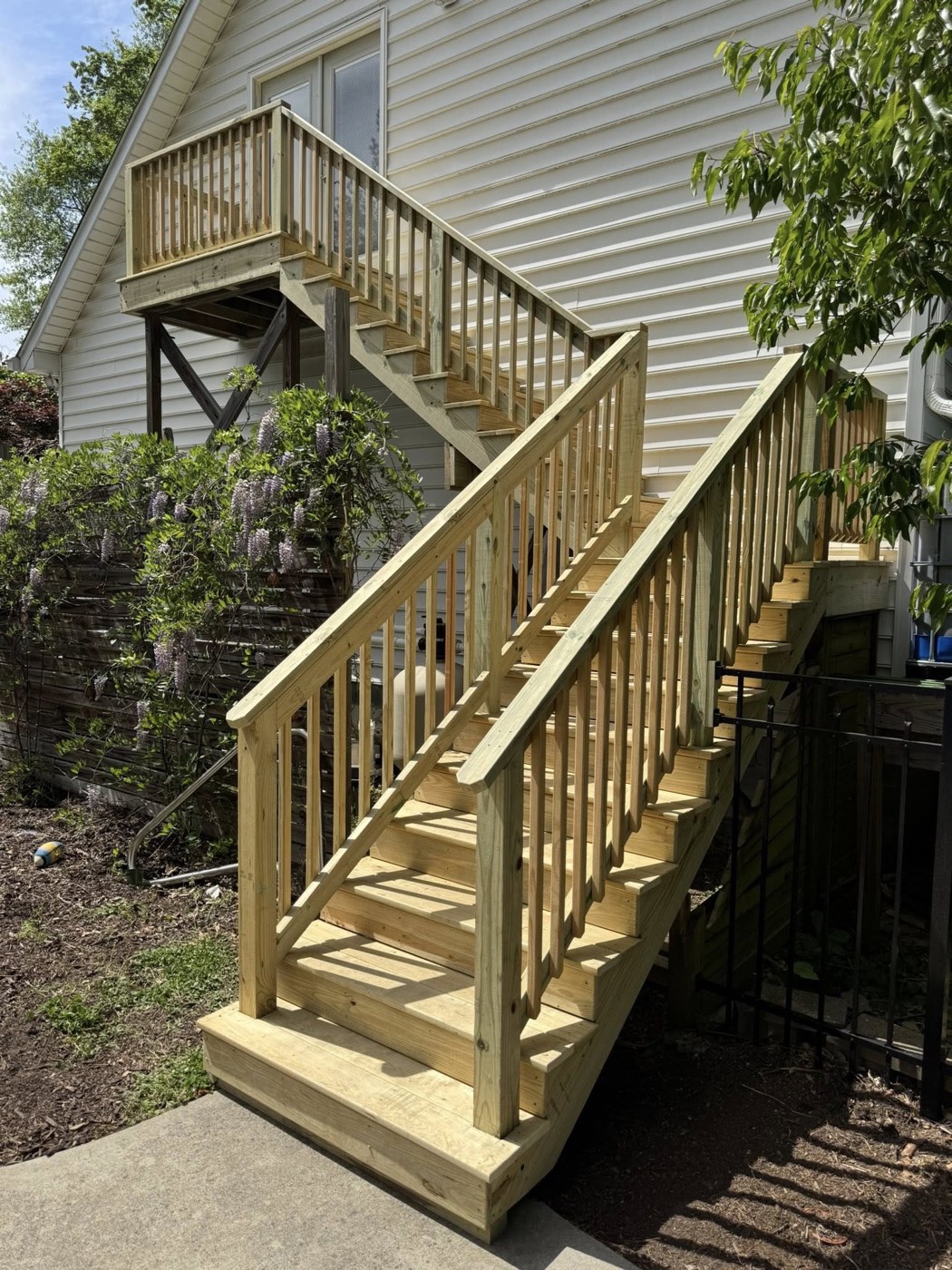 A pressure-treated staircase and landing carrying a raised deck down to grade, framed square with clean rails and stringers.