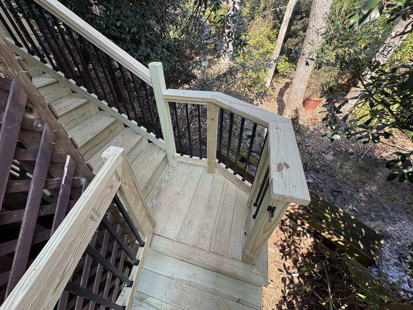 A fresh pressure-treated deck landing and stair turn on a wooded lot — solid footing and a clean handrail on a tricky grade.