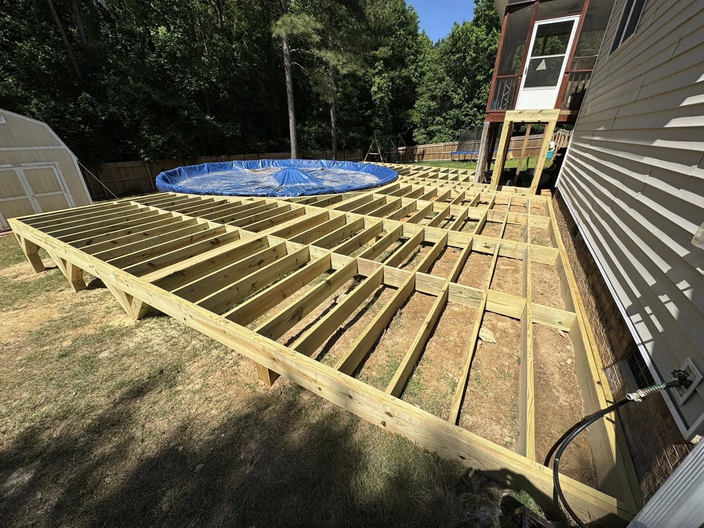 Framing and joists going in for a wraparound pool deck — the structural work that decides whether a deck stays solid and level.