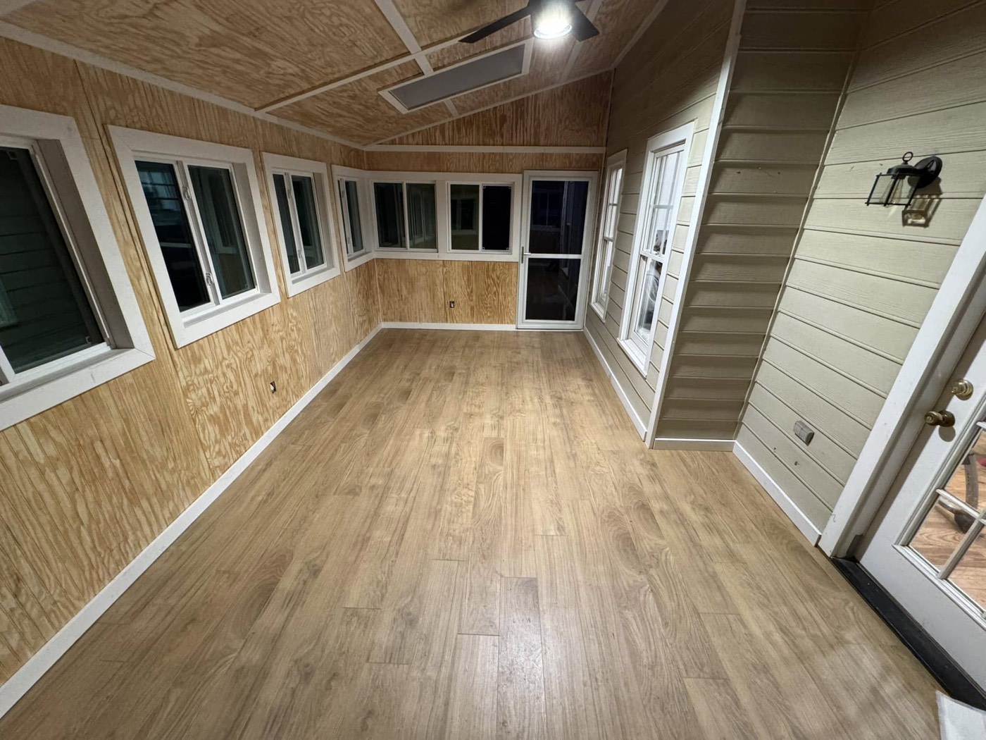 Inside a finished screened porch — a warm wood ceiling, wood-look flooring and full-height screens, built as a genuine outdoor room.
