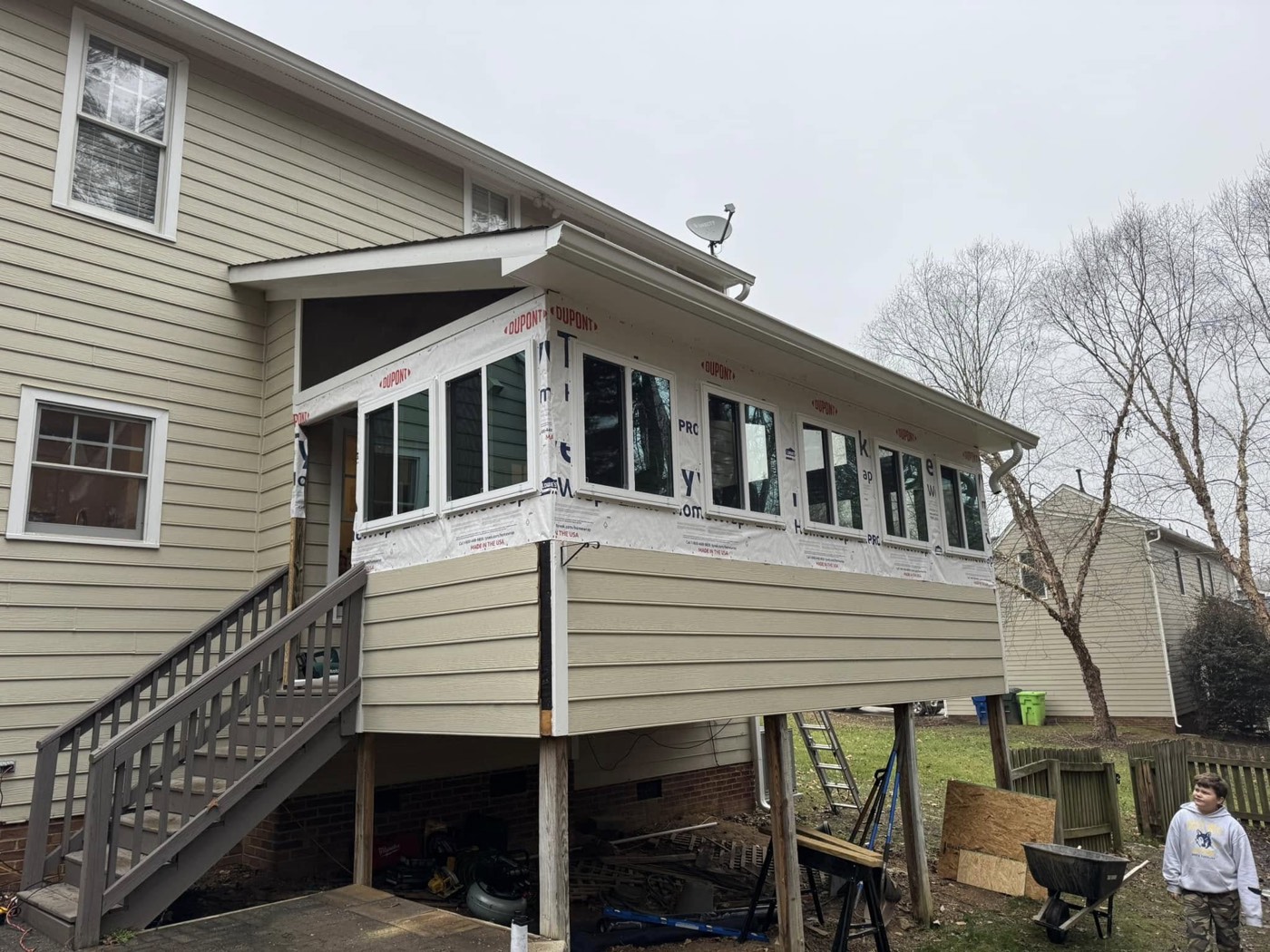 A porch and outdoor-room addition mid-build, framed and wrapped ahead of siding — construction work that goes beyond decking.